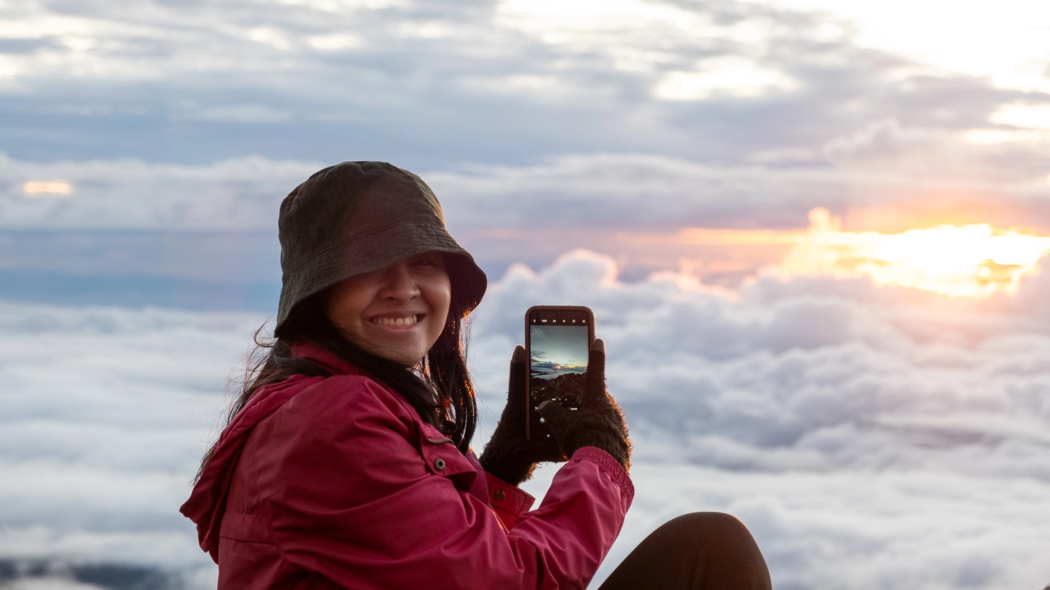 A hiker smiling as she takes a picture of sunrise at Mt. Apo Boulder Face