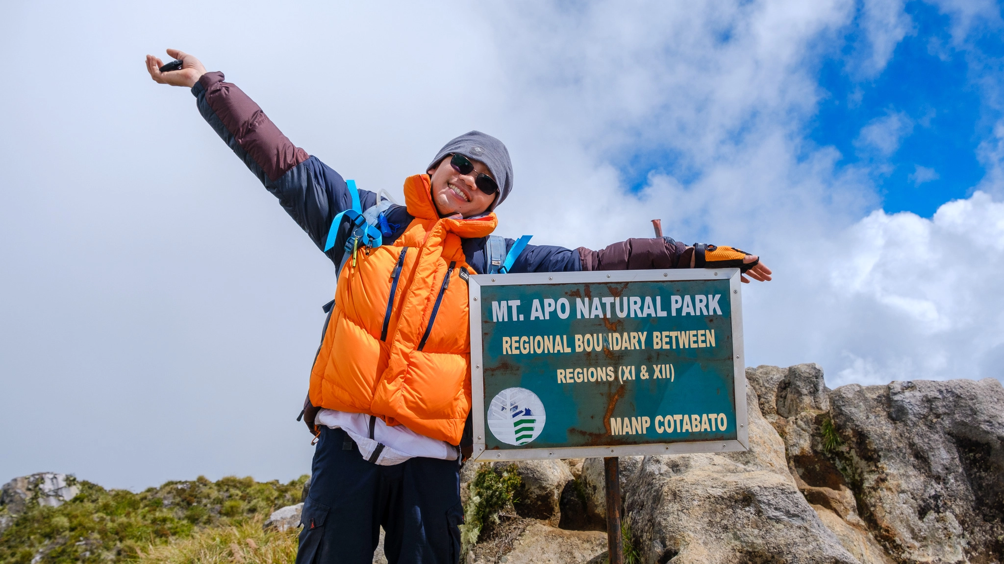 A hiker smiling at the Mt. Apo summit sign