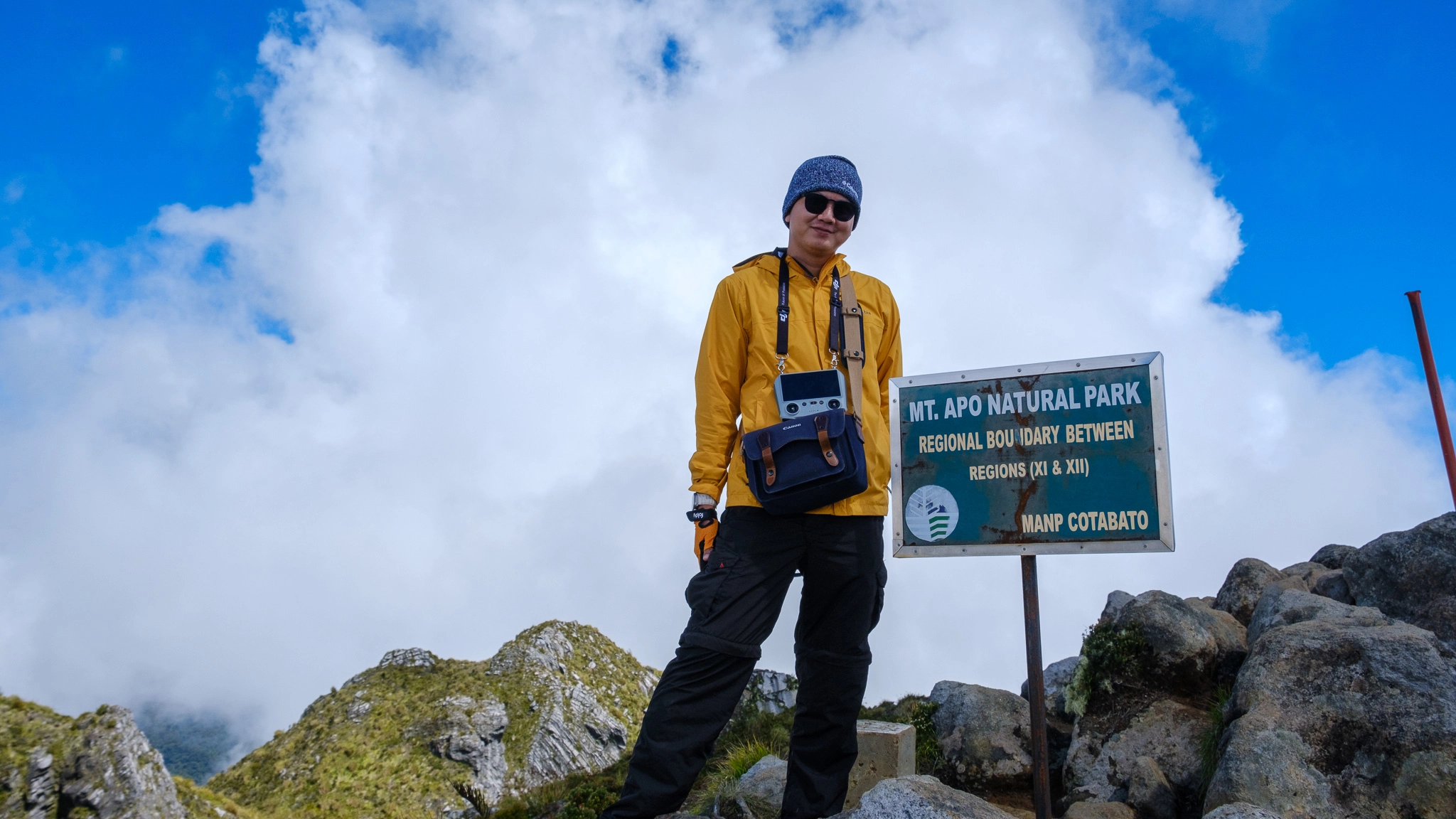 A hiker smiling at the Mt. Apo summit sign