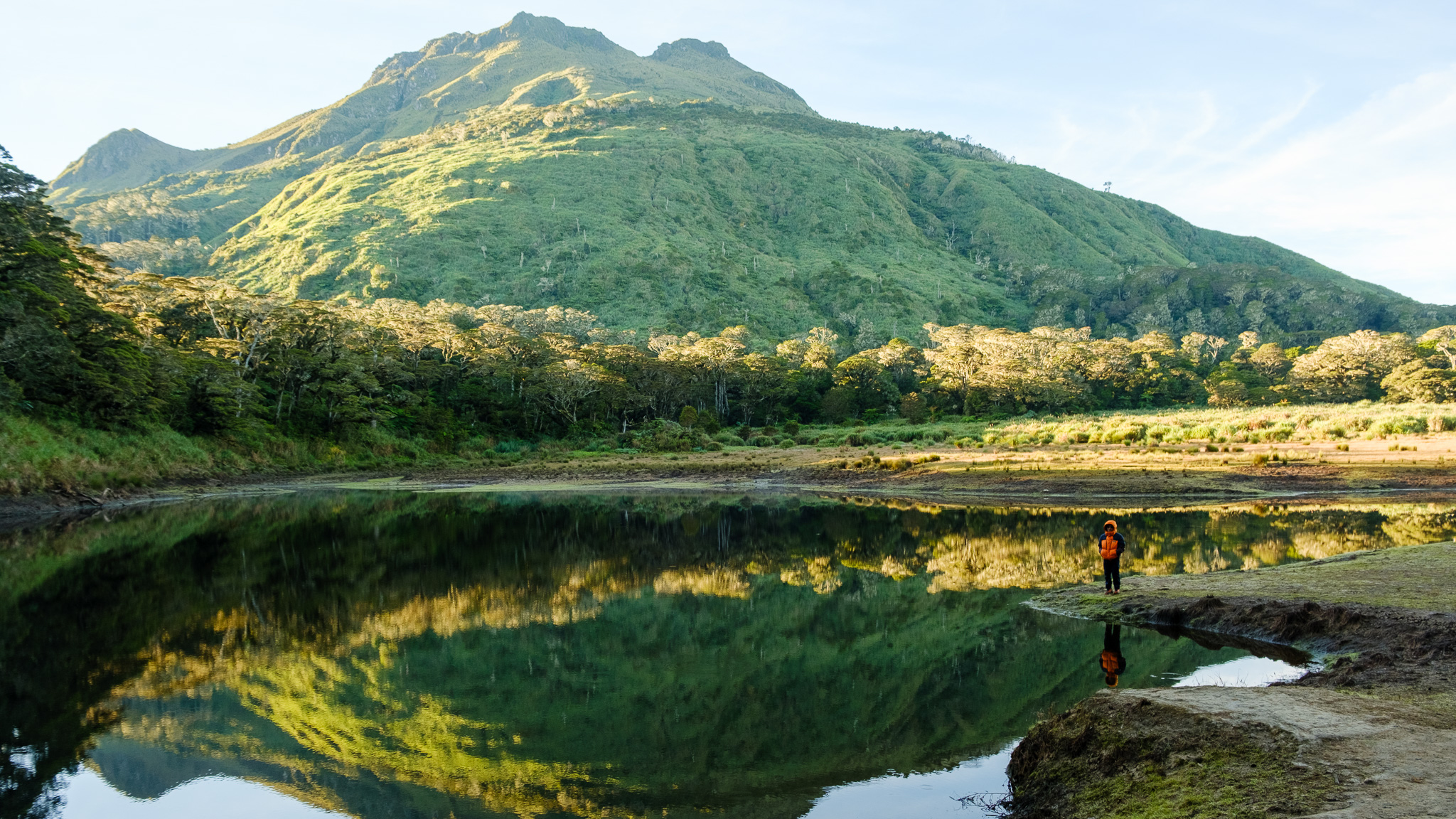 A person standing at Lake Venado with Mt. Apo on his background, and the lake reflecting Mt. Apo